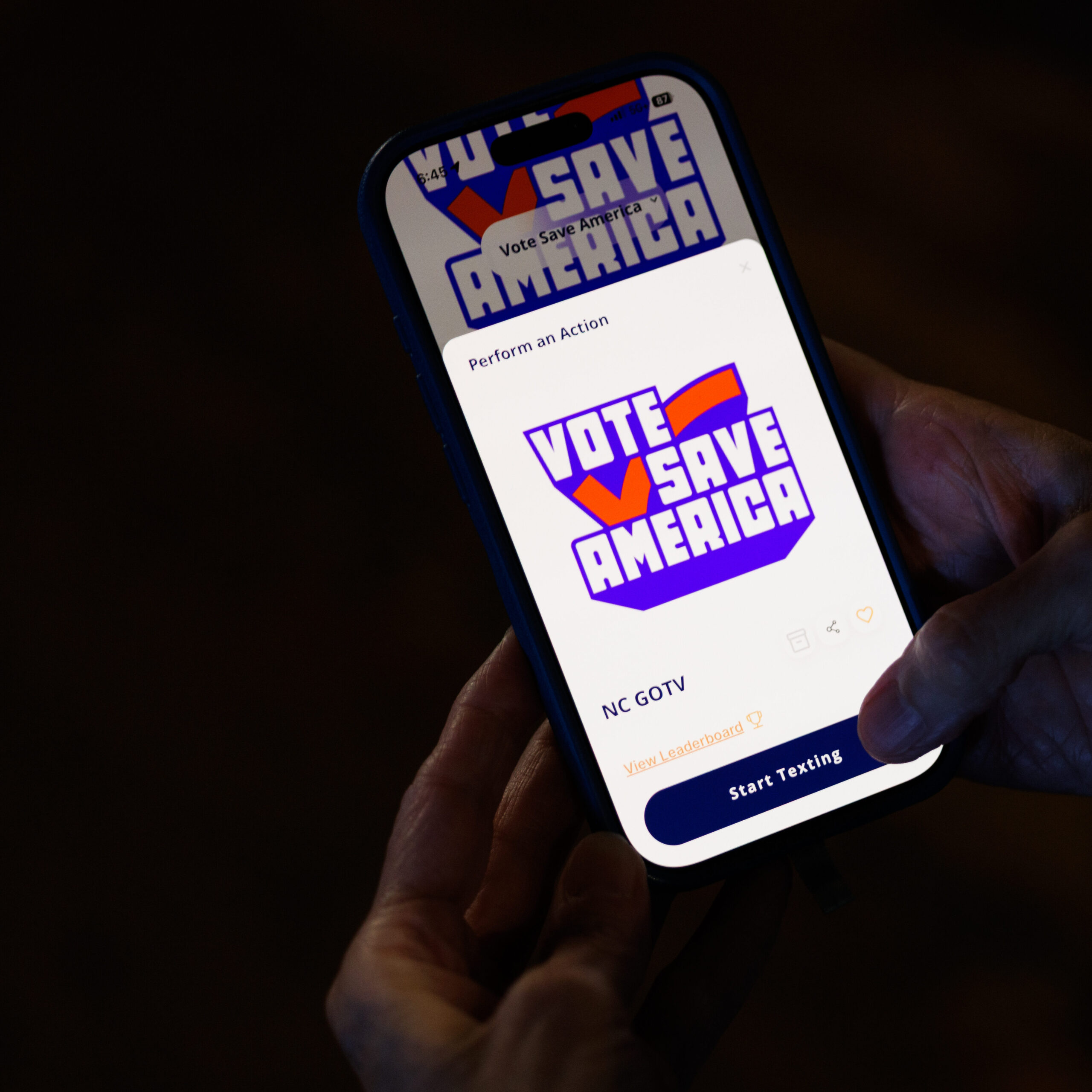 A phone screen showing the Vote Save America logo glows in the dark.